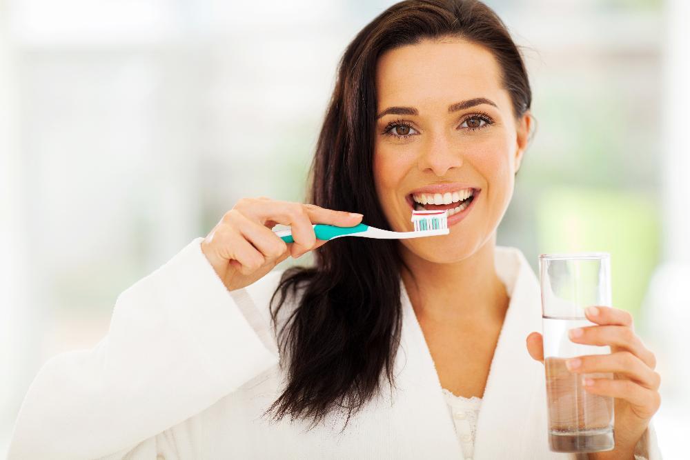 A smiling woman brushing her teeth | dental crowns Brandon FL