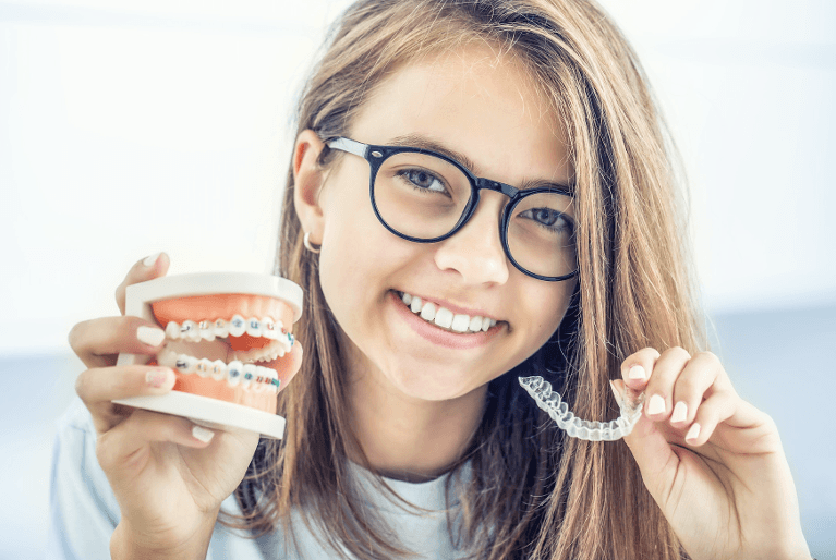 A girl holding an orthodontic model with braces and an Invisalign tray