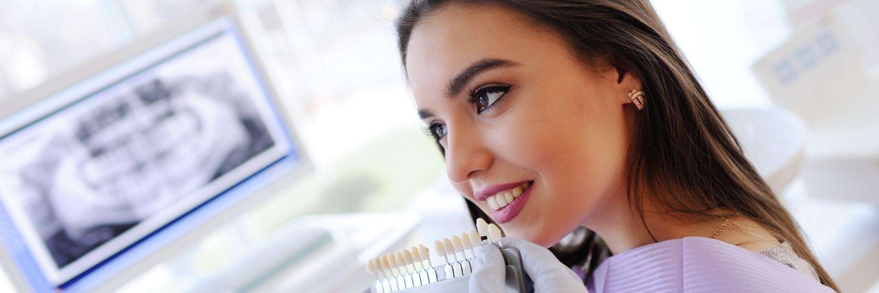 A woman comparing tooth color shades at the dentist